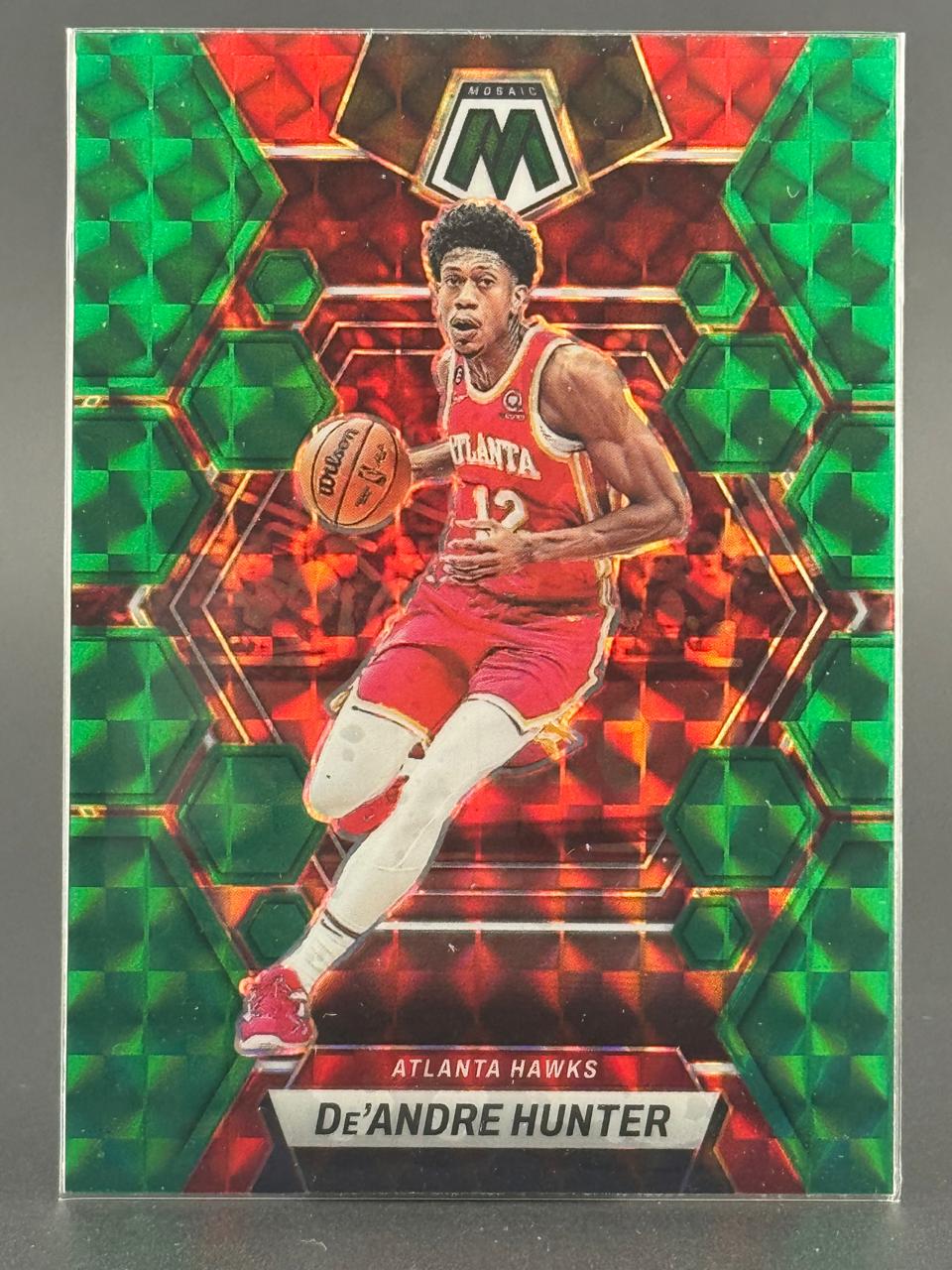 2022-23 Panini Mosaic De'Andre Hunter trading card in red and green holo finish, featuring him dribbling for the Hawks.