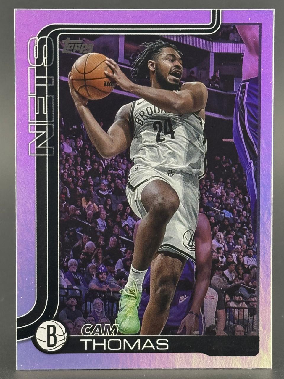 Trading card of Cam Thomas in a Nets uniform holding a basketball, with a purple border.