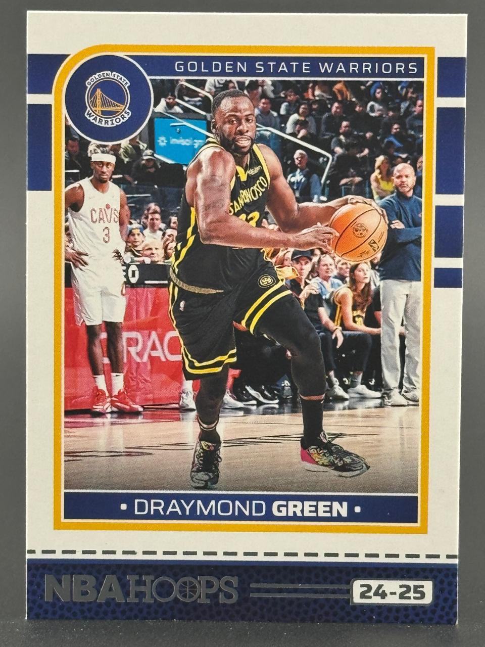24-25 NBA Hoops basketball trading card of Draymond Green dribbling in a Golden State Warriors uniform.