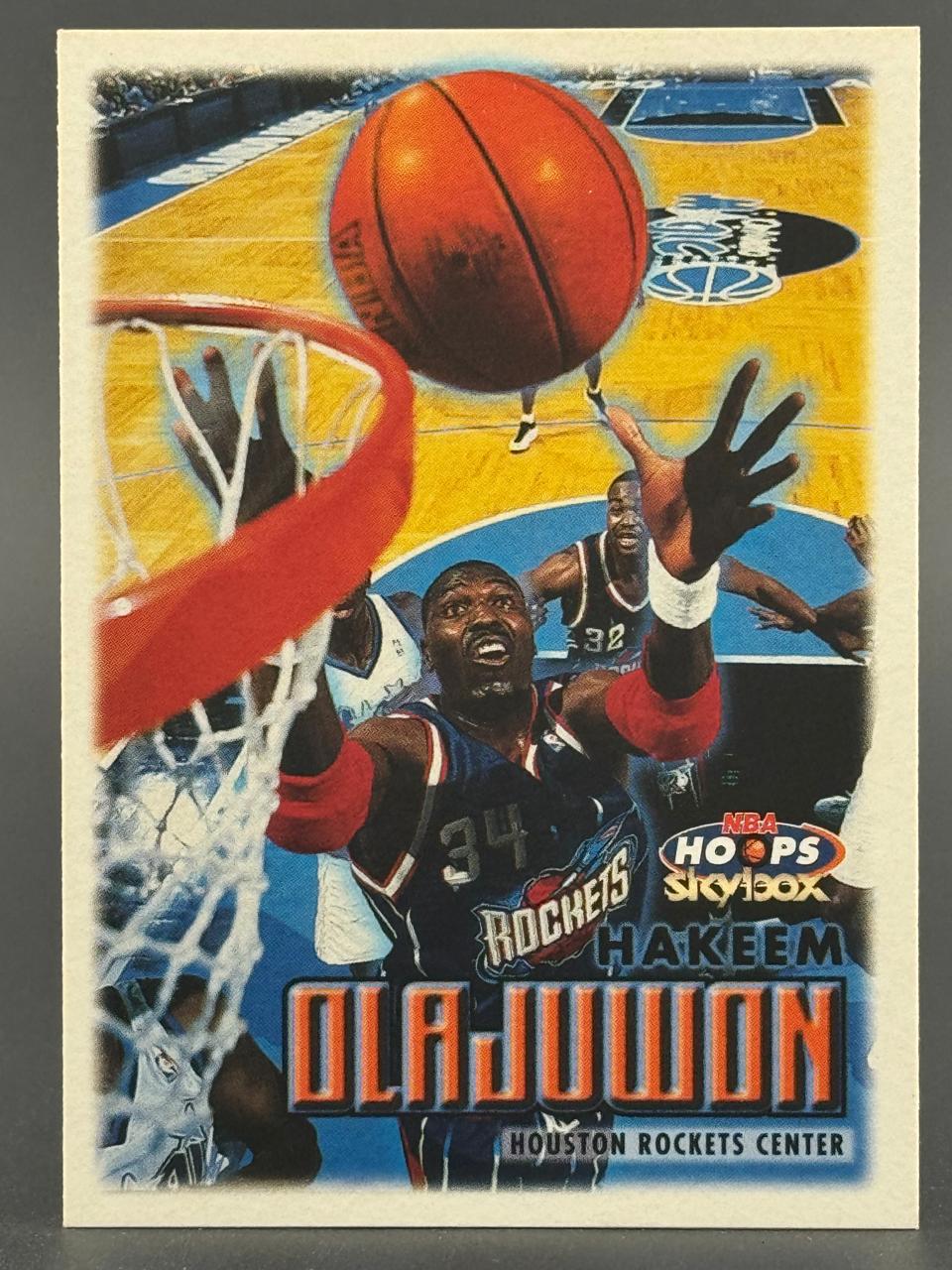 Hakeem Olajuwon 1996-97 NBA Hoops SkyBox trading card #34, showing him playing for the Houston Rockets.