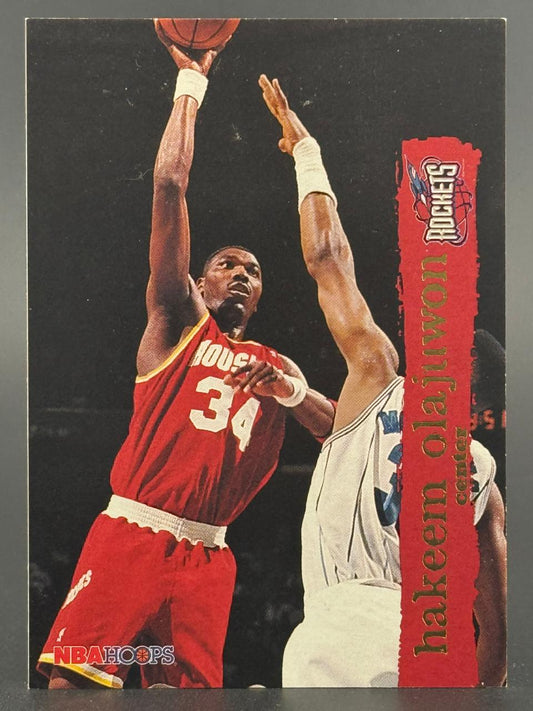 Hakeem Olajuwon shooting a basketball on a red and gold 1993-94 NBA Hoops card.