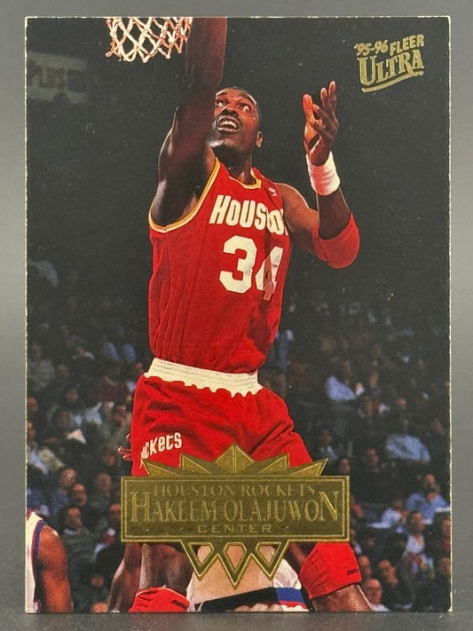 1995-96 Fleer Ultra Hakeem Olajuwon basketball card featuring him shooting a layup in a Rockets uniform.