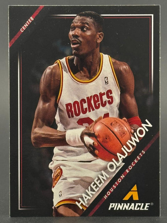 Hakeem Olajuwon basketball trading card, Pinnacle brand, showing him holding a basketball in a Rockets jersey.