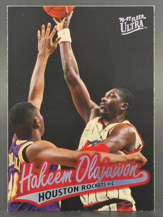 1996-97 Fleer Ultra Hakeem Olajuwon basketball card featuring him shooting over an opponent.