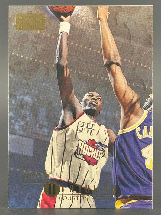 Hakeem Olajuwon basketball trading card, showing him in a Houston Rockets uniform shooting over an opponent.
