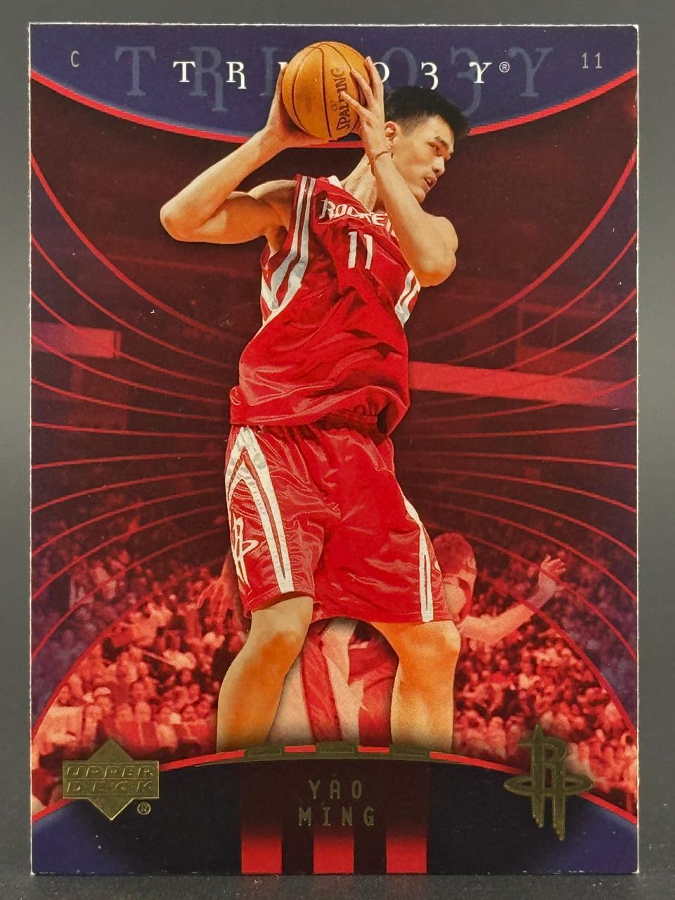 Yao Ming 2003 Upper Deck Trilogy trading card #11, showing him holding a basketball in a red Rockets uniform.