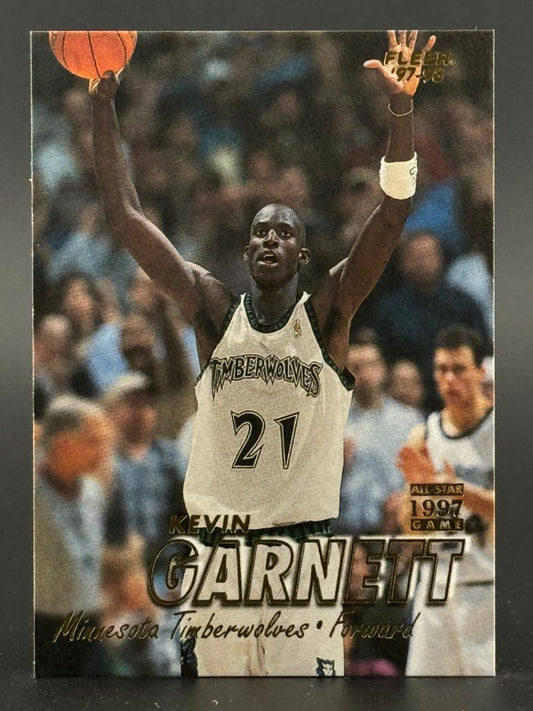 1997-98 Fleer Kevin Garnett trading card showing him holding a basketball with both arms raised.
