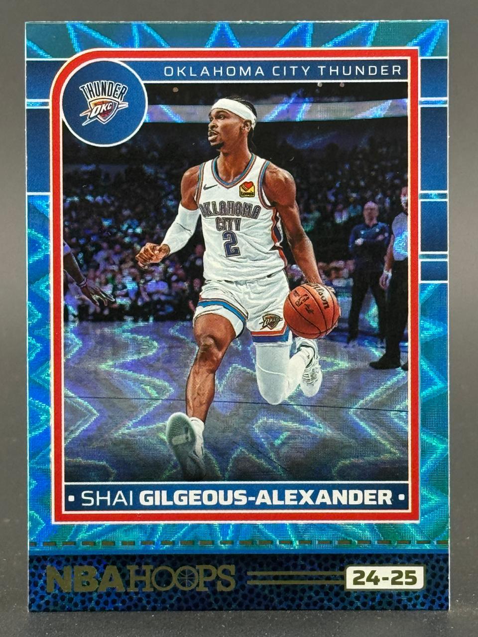 2024-25 NBA Hoops Shai Gilgeous-Alexander trading card with a blue holographic border.