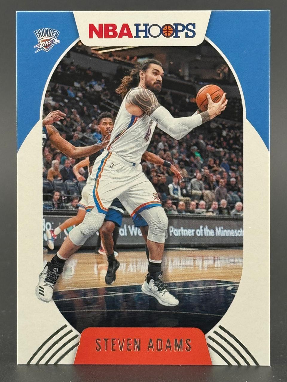 Steven Adams basketball trading card, NBA Hoops set, showing him holding a basketball on the court.