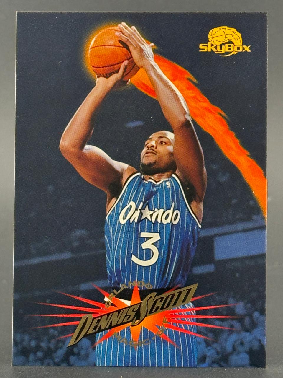 1990s SkyBox basketball trading card of Dennis Scott in an Orlando Magic uniform, holding a basketball with a flame graphic.