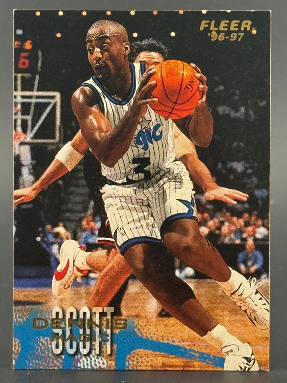 1996-97 Fleer Dennis Scott basketball card featuring him dribbling in an Orlando Magic uniform.