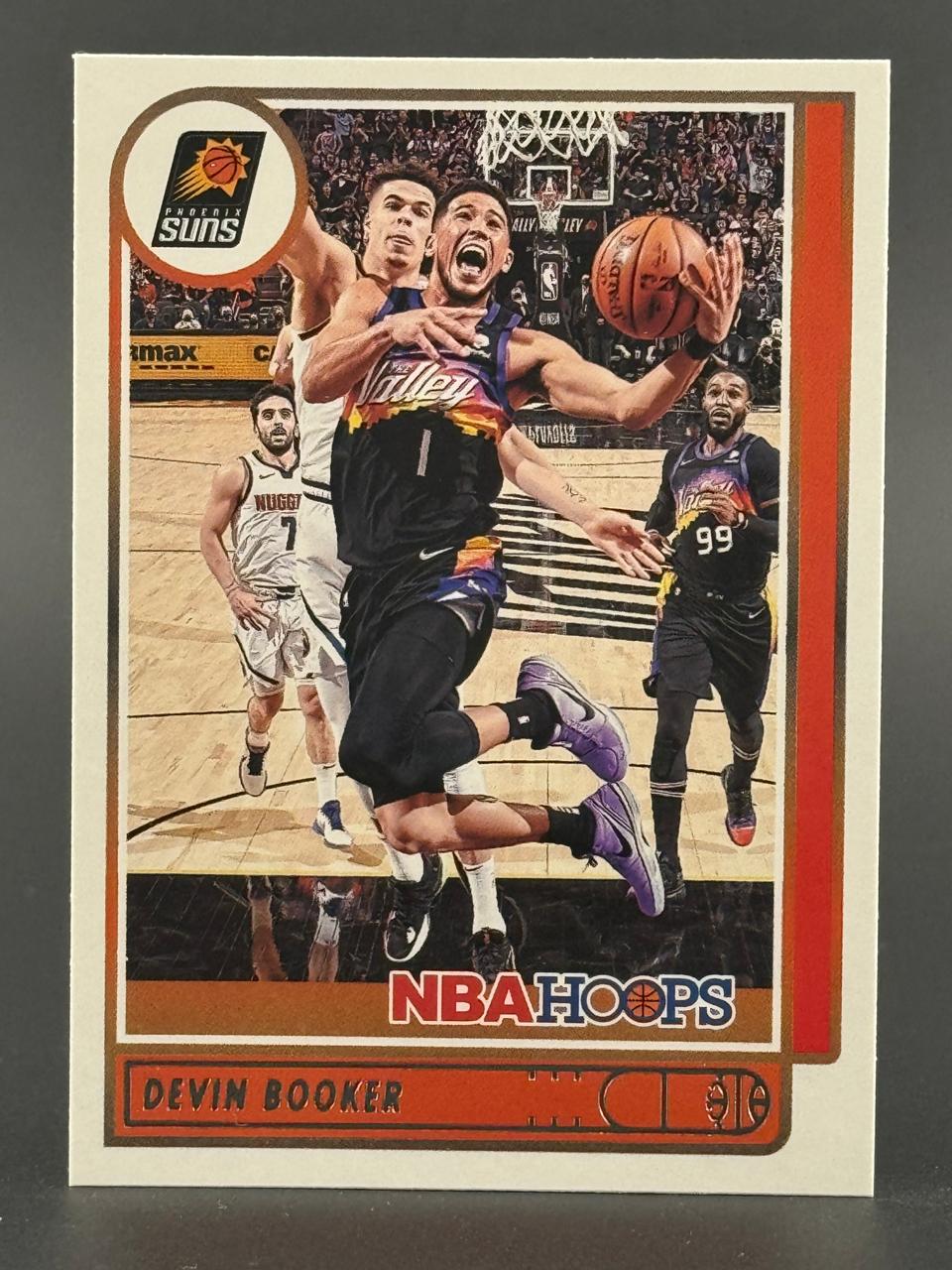 Devin Booker 2020-21 NBA Hoops trading card featuring Booker driving the lane in a Phoenix Suns uniform.
