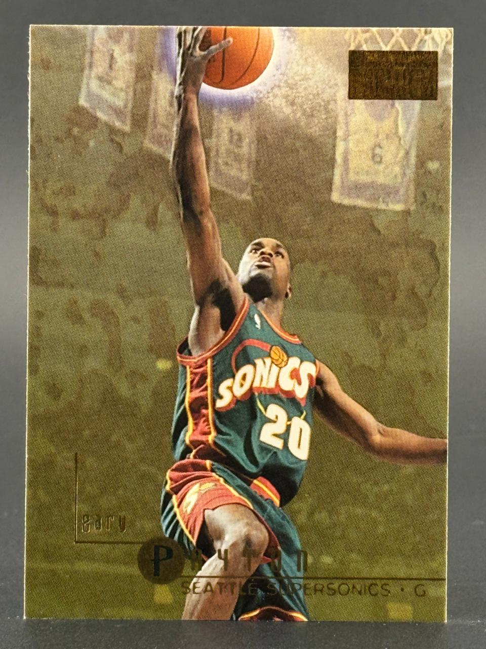 Trading card of Gary Payton in a Seattle SuperSonics uniform, reaching up to dunk a basketball.