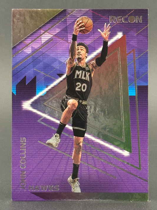 John Collins 2021-22 Panini Recon basketball card showing him shooting a layup in a black Hawks MLK uniform.