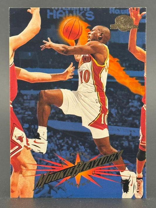 Trading card of Mookie Blaylock in a white Atlanta Hawks uniform driving with a basketball, surrounded by defenders.